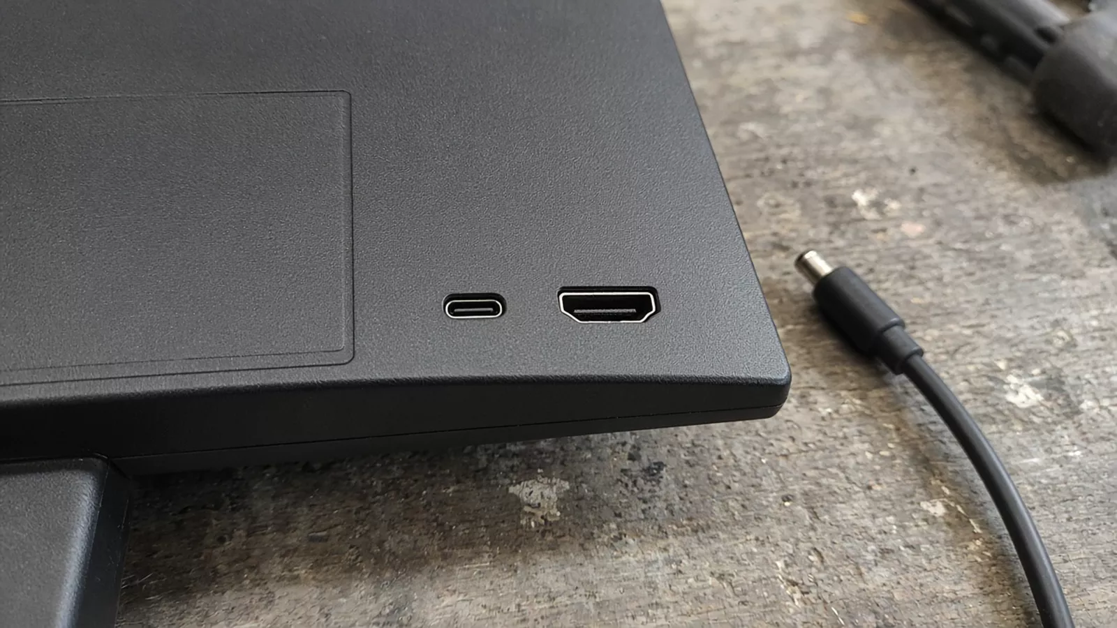 Two empty ports of different shapes on a monitor edge, with an unplugged round-plug cable beside them